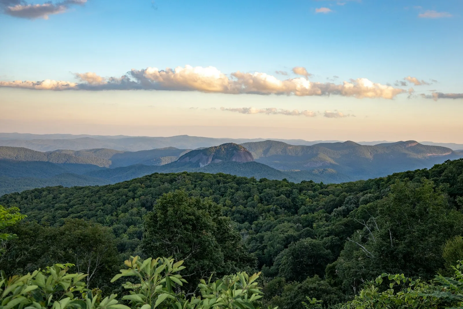 The Blue Ridge Mountains outside Asheville at golden hour: forested ridges rolling back to the rounded dome of Looking Glass Rock under a streak of cloud