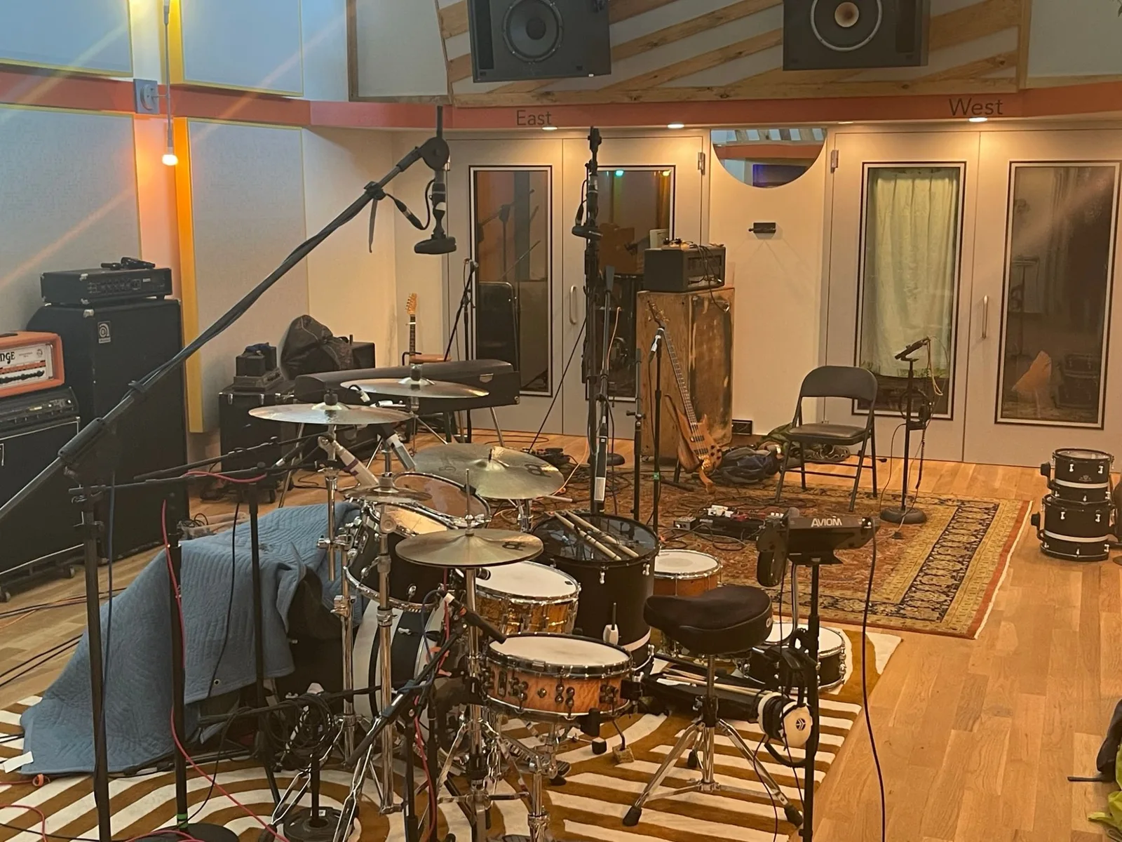 The live room at the Asheville studio set for a session: a drum kit under a boom mic, amps along the wall, a bass leaning on its cabinet, and a rug at the center of the floor